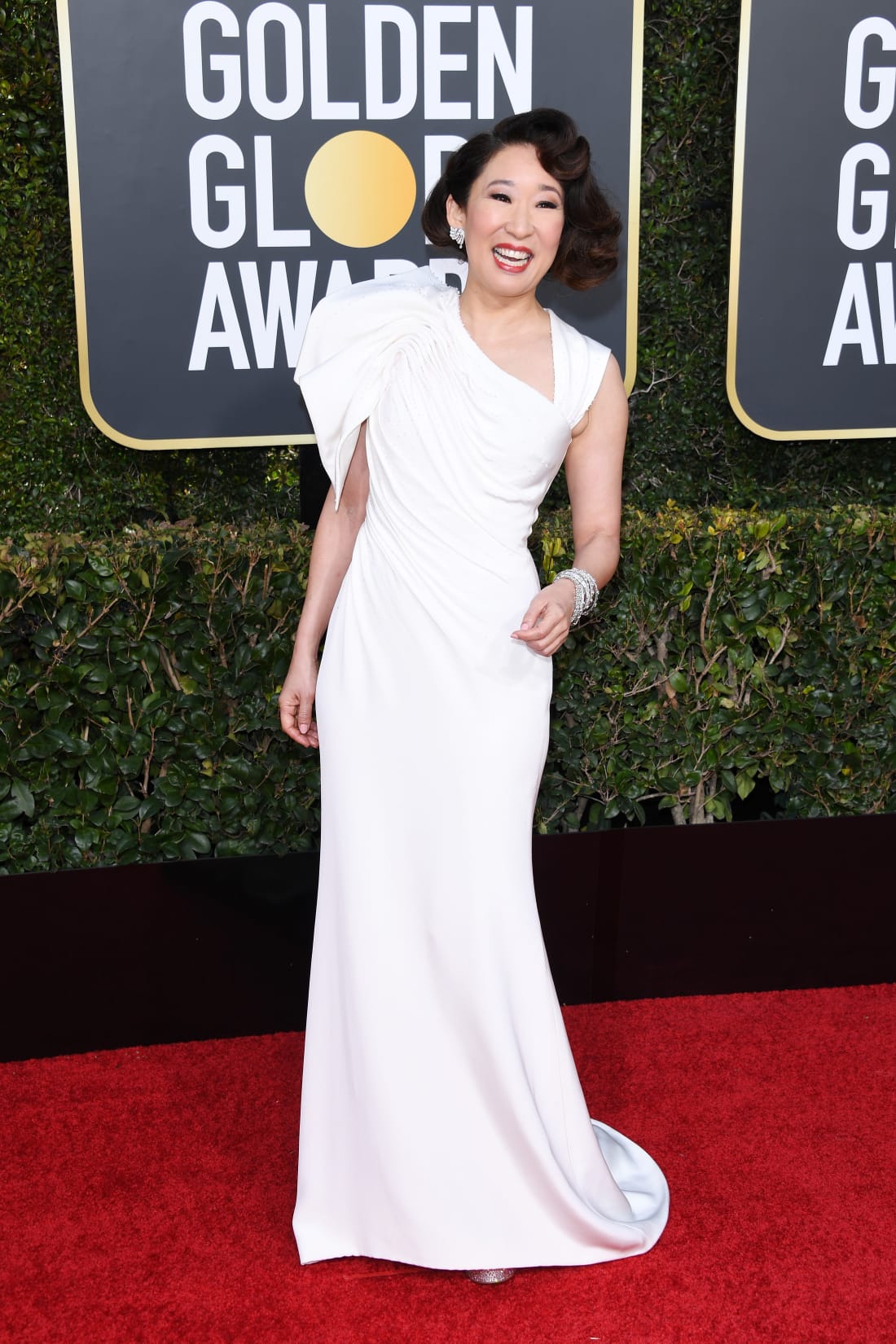 Sandra Oh channeled vintage Hollywood glamour with side-swept curls and red lips. She wore a draped ivory dress by Versace.